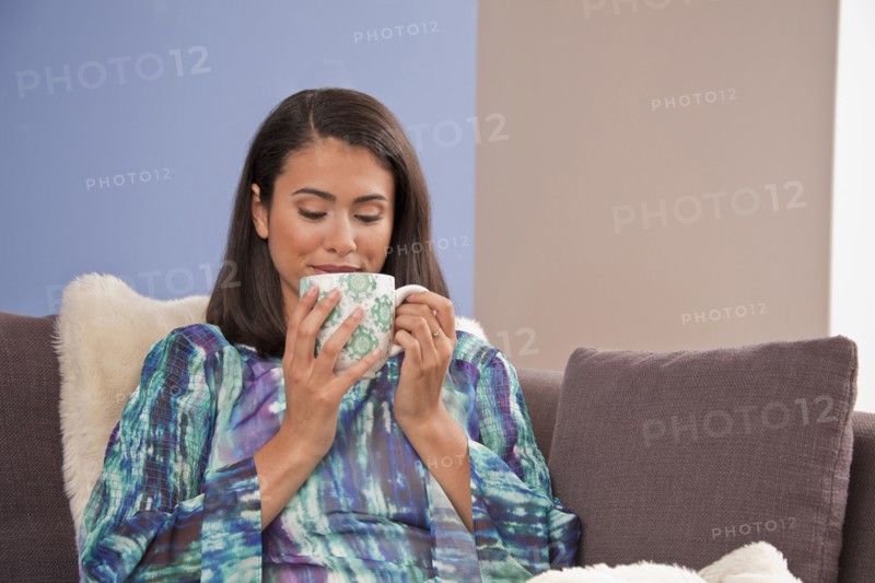 Hispanic woman sitting on sofa drinking warm beverage
