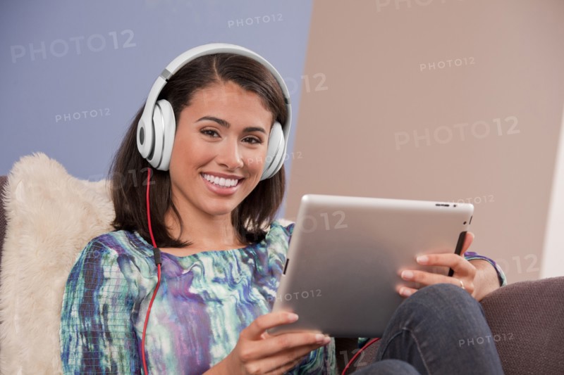 Smiling Hispanic woman sitting on sofa with digital tablet
