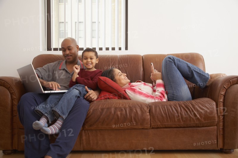 Antiguan man using laptop in living room with family