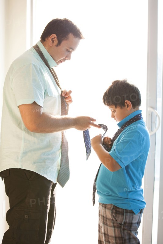 Hispanic father showing son how to tie necktie