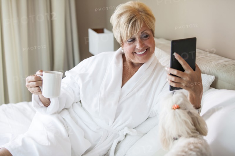 Older Caucasian woman and dog using digital tablet on bed