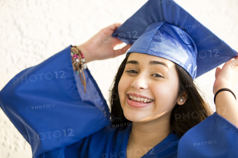 Smiling Hispanic girl wearing graduation robe and mortarboard