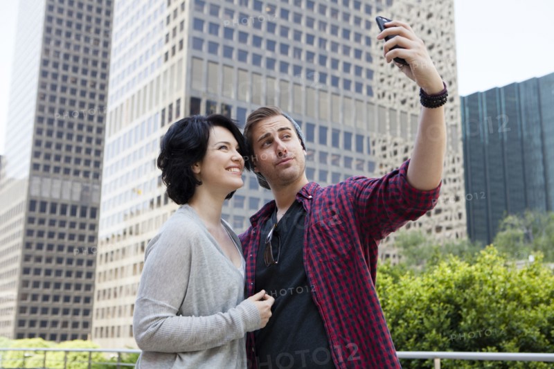 Caucasian couple taking selfie with cell phone in city