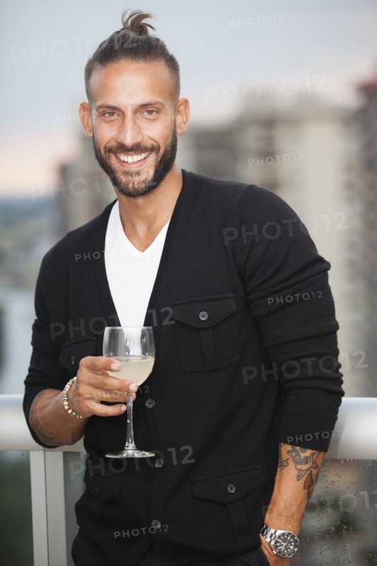 Hispanic man drinking wine on urban balcony