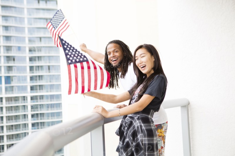 Couple waving American flags on urban balcony