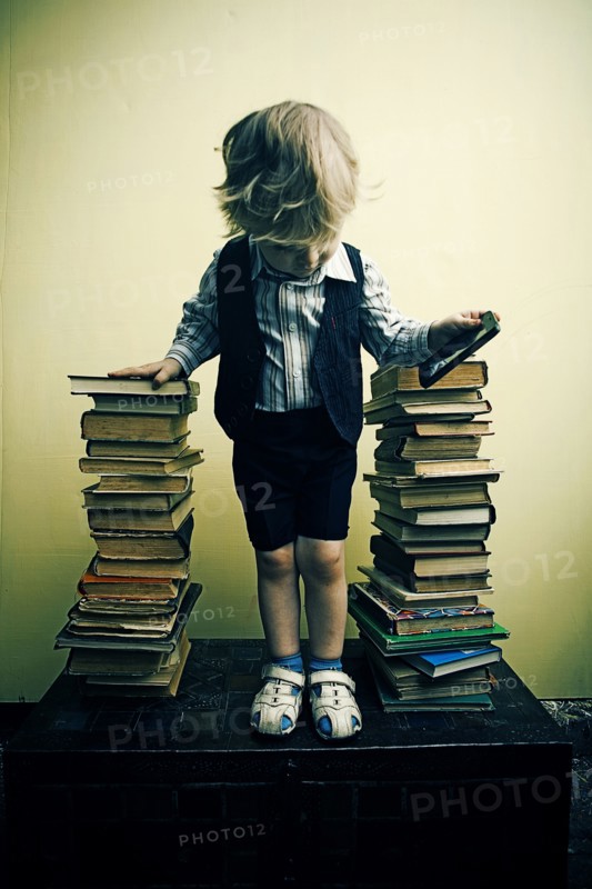 Boy holding cell phone near stacks of books