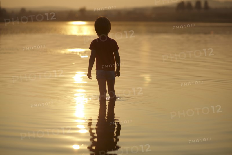 Silhouette of boy standing in pond at sunset