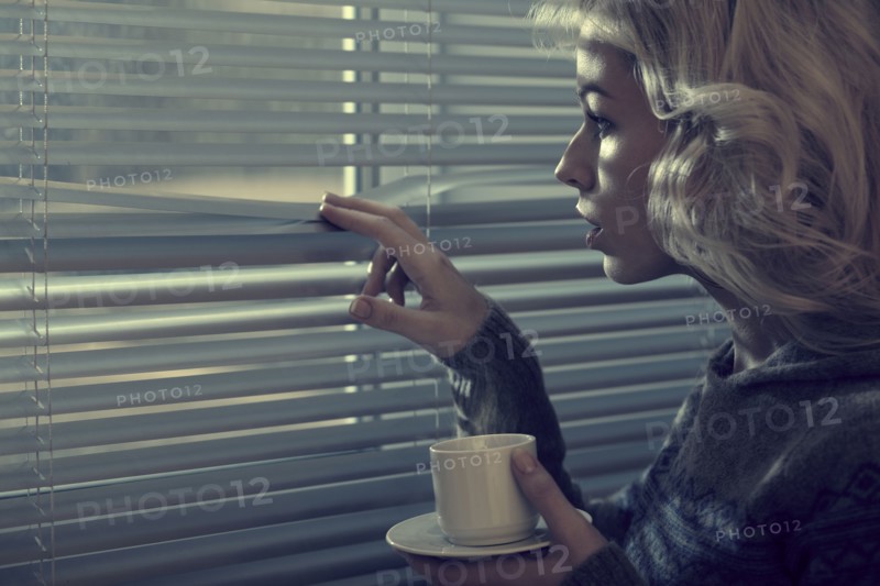 Caucasian woman peering through blinds