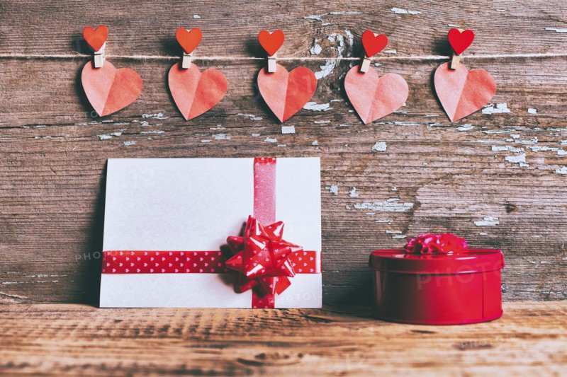 Valentine hearts hanging on string above gift box and card