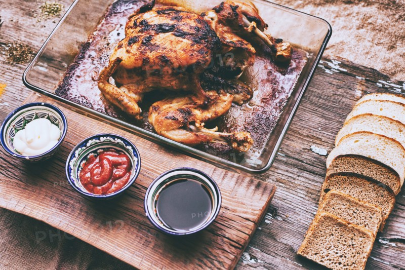 Close up of roasted chicken with bread and sauces on wooden table