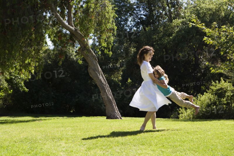 Mother swinging daughter in park