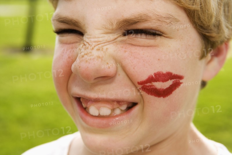 Grimacing boy with lipstick kiss on face