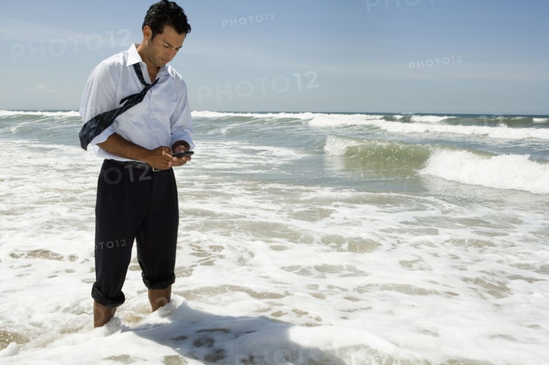 Businessman text messaging on cell phone while standing in ocean