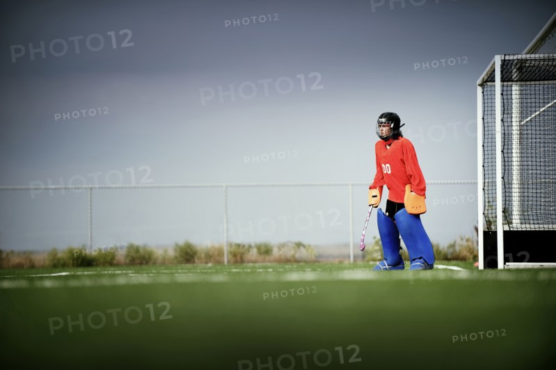 Mixed race field hockey goalie standing by goal