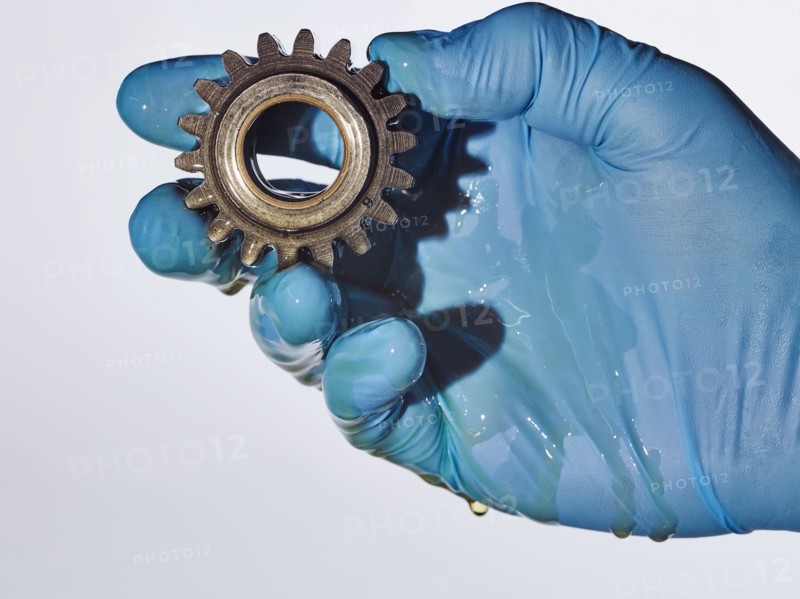 Hand wearing rubber-glove holding gear dripping with oil