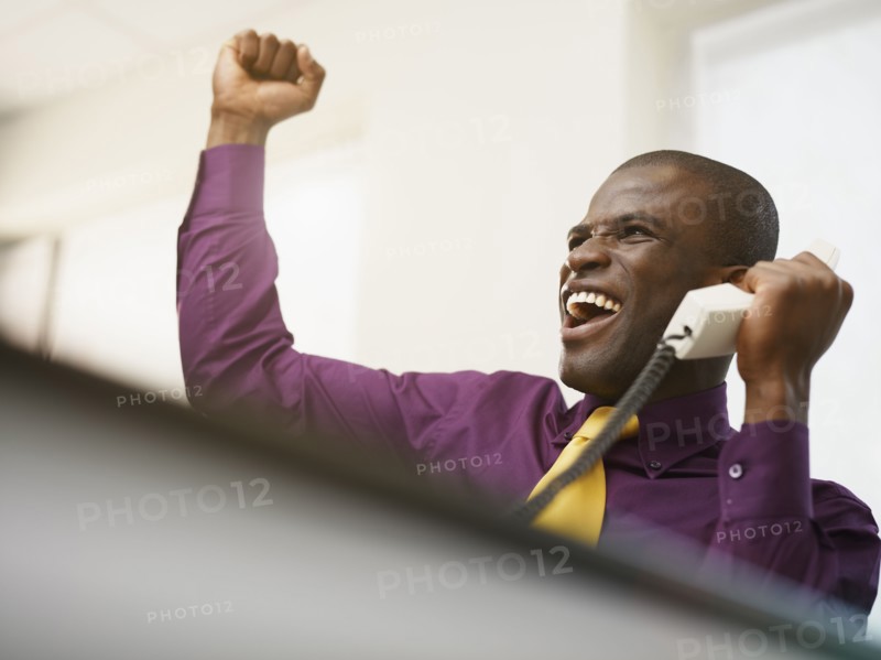 Cheering Black businessman holding telephone