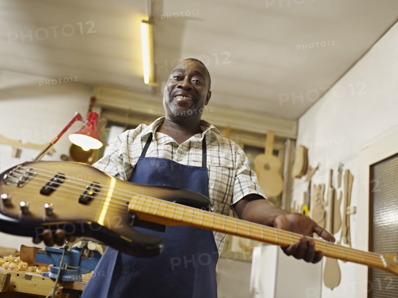 Black craftsman holding electric guitar in workshop