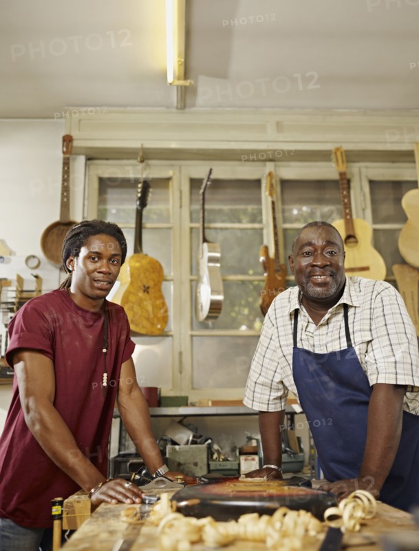 Black craftsman in guitar workshop with son