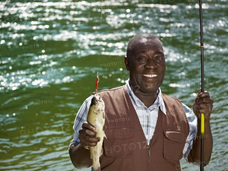 Black man holding fish and fishing rod near stream