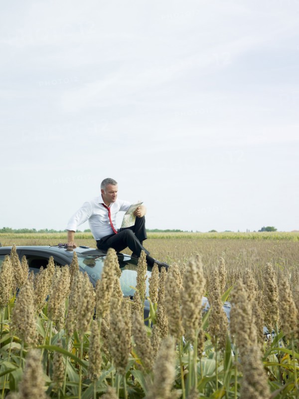 Caucasian businessman sitting on top of car in field