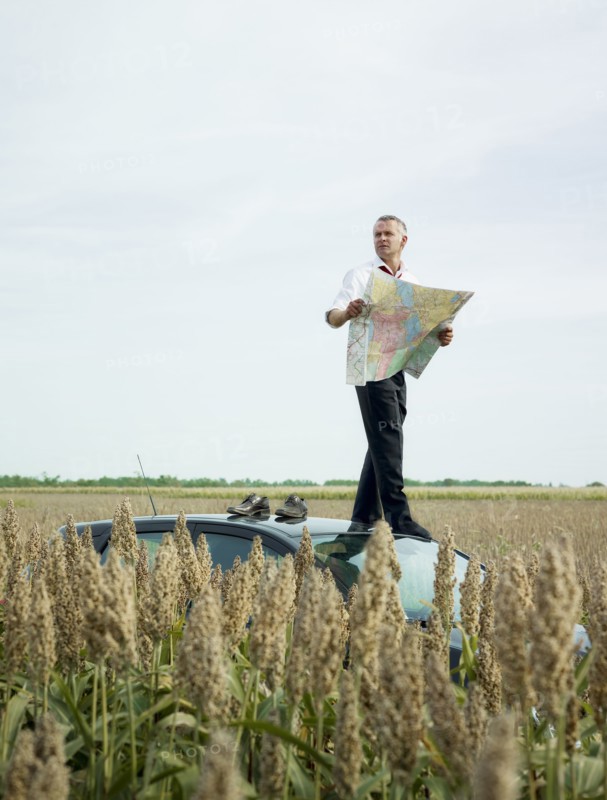 Caucasian businessman on top of car in field looking at map