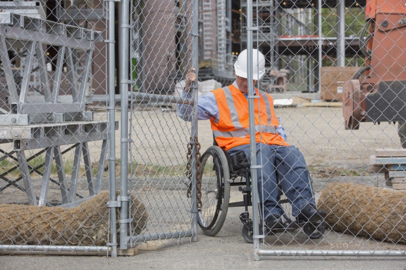 Caucasian engineer in wheelchair opening construction site gate