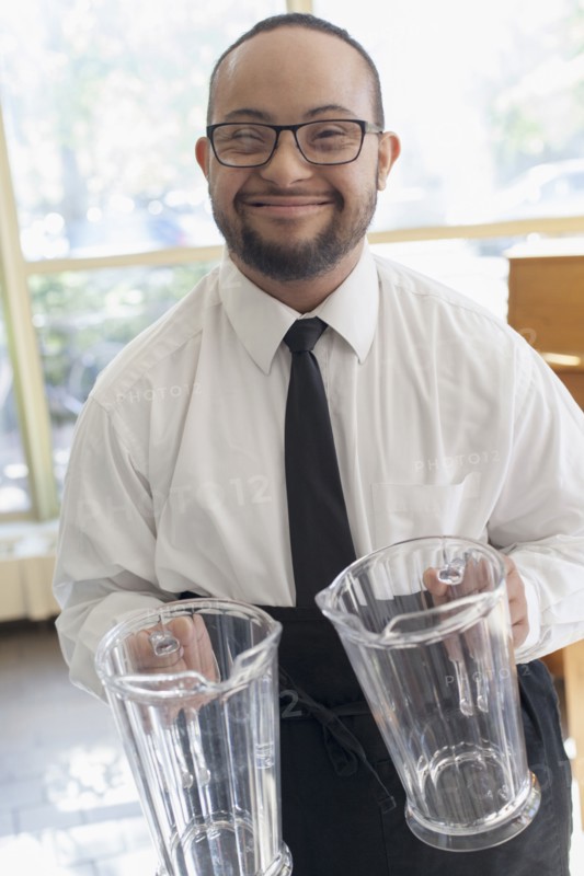 Mixed race server with down syndrome holding pitchers in restaurant
