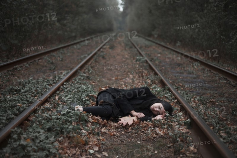 Caucasian woman laying between railroad tracks