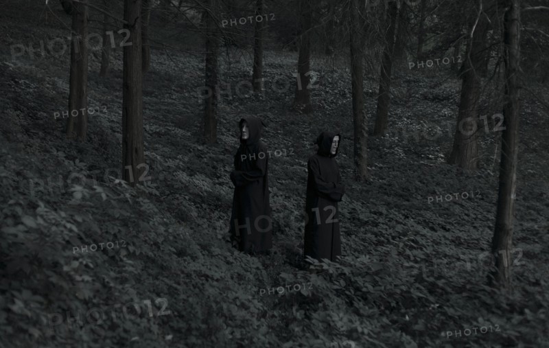 People wearing black robes and white masks in forest