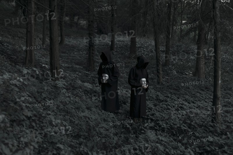 People wearing black robes and holding white masks in forest