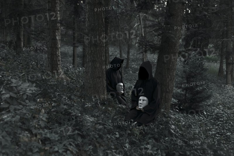 People wearing black robes and holding white masks sitting in forest