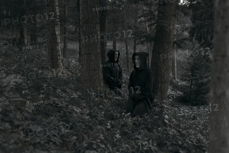 People wearing black robes and white masks sitting in forest