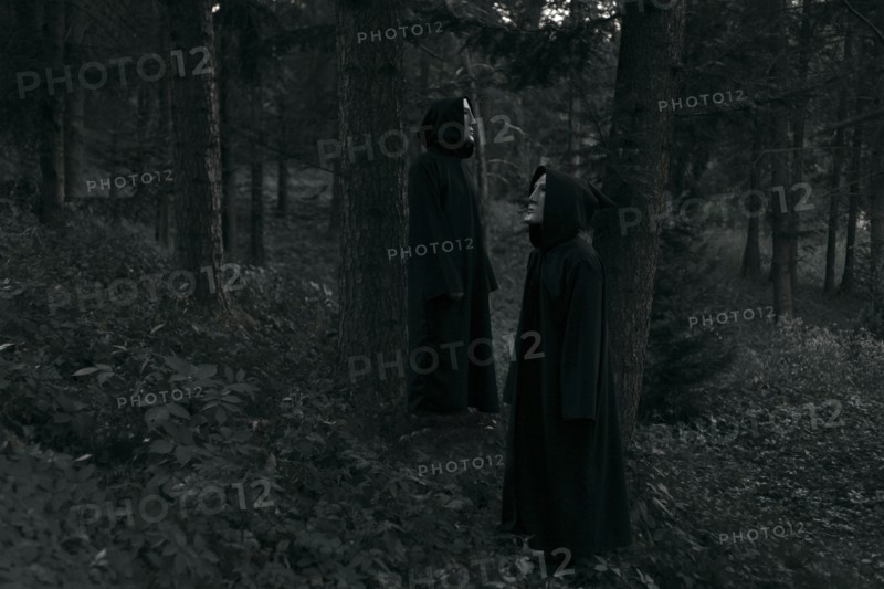 People wearing black robes and white masks standing in forest