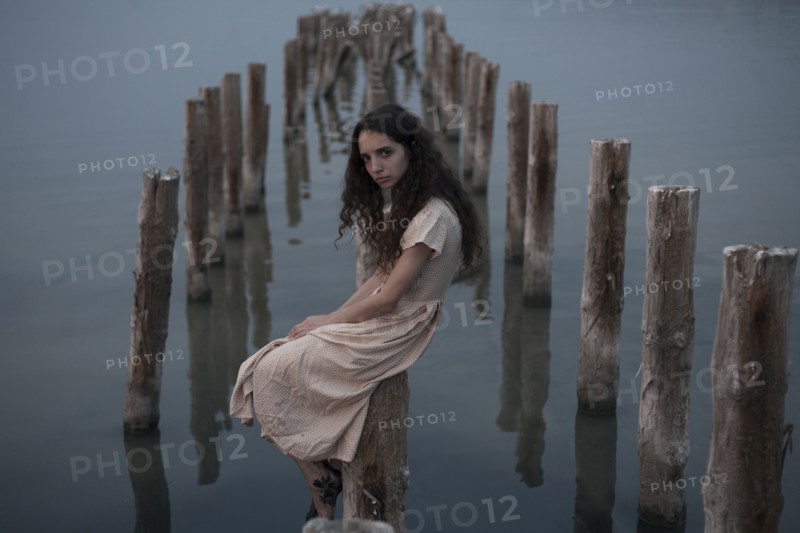 Serious Caucasian woman sitting on piling in river