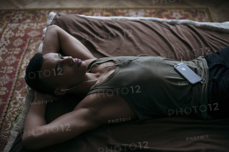 Black man laying on bed listening to music on cell phone