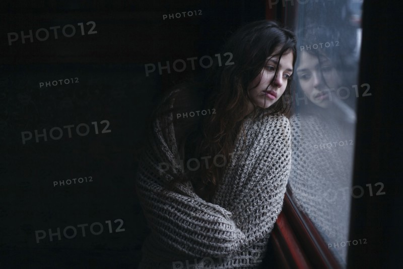 Sad Caucasian woman wrapped in scarf leaning on window