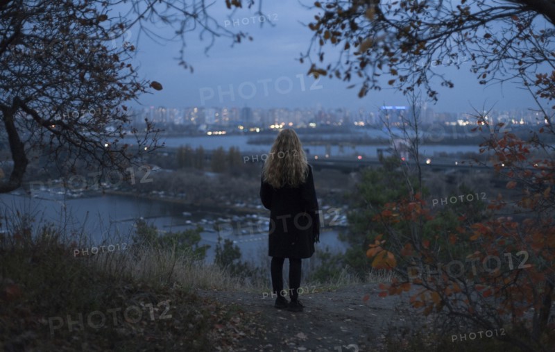 Pensive Caucasian woman standing near urban waterfront at night