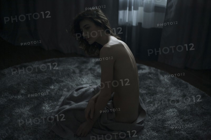 Portrait of nude Caucasian woman sitting on rug with blanket