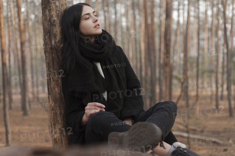 Pensive Caucasian woman sitting on log in forest