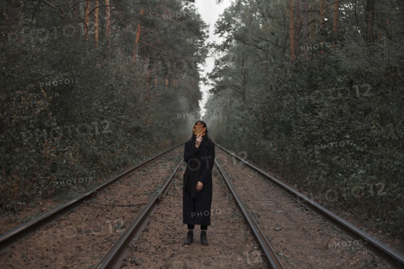 Caucasian woman holding autumn leaf on train tracks in forest