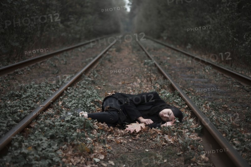 Caucasian woman laying on autumn leaves near train tracks in forest
