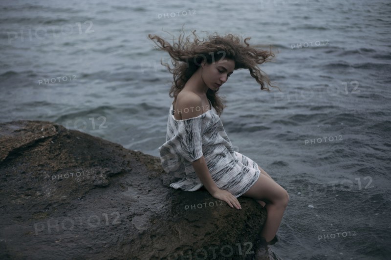 Wind blowing hair of Caucasian girl sitting at ocean