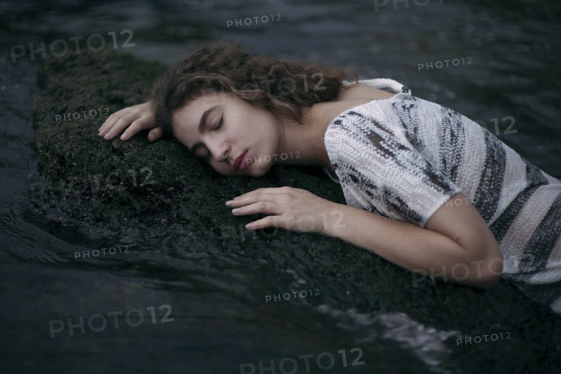 Caucasian girl laying face on a rock in ocean