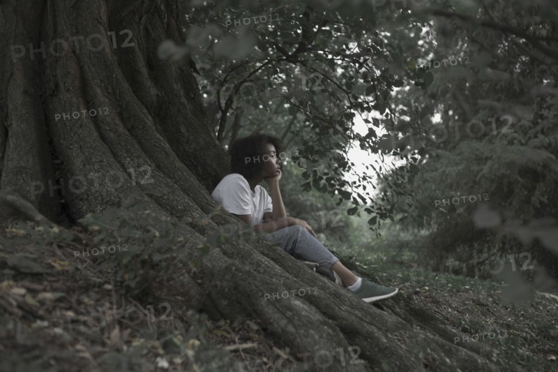 Pensive woman sitting on tree roots in forest
