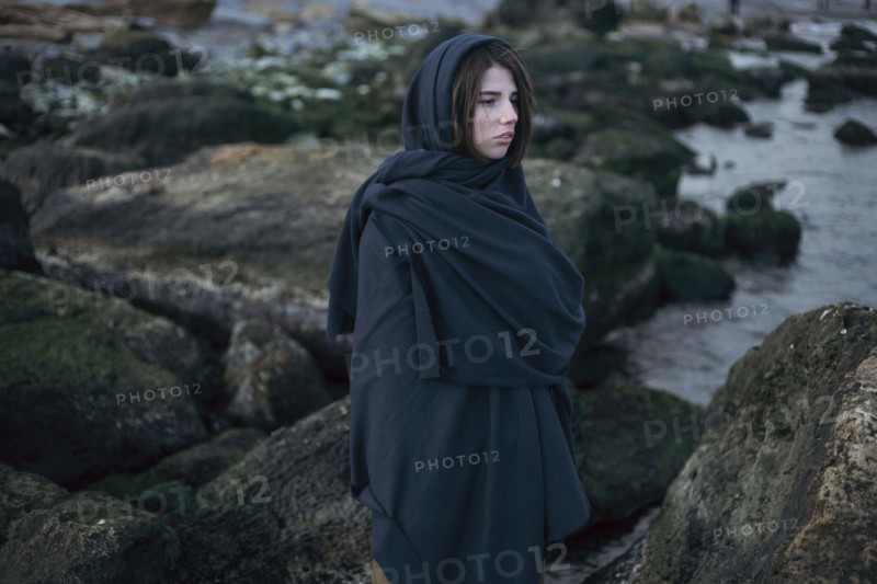 Caucasian woman wearing scarf on rocks at ocean