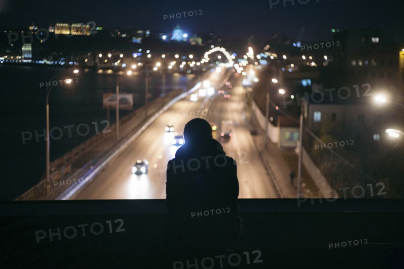 Silhouette of person watching traffic from overpass at night