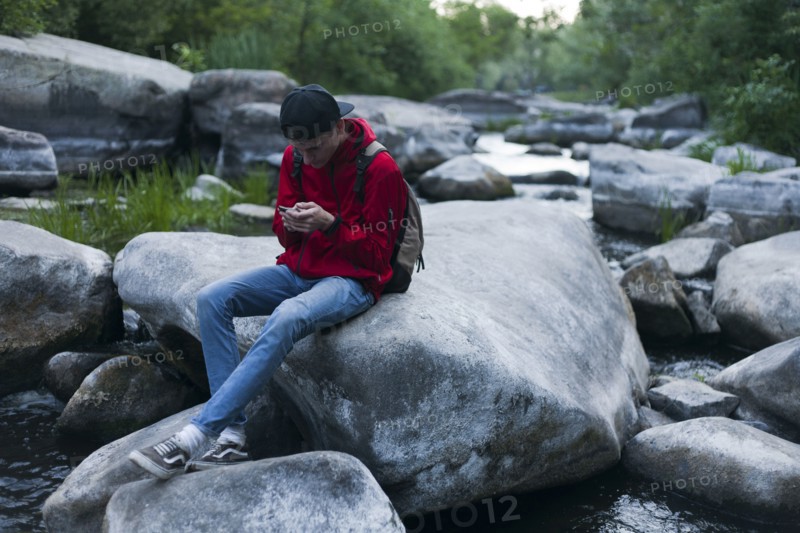 Caucasian man sitting on rock in river texting on cell phone