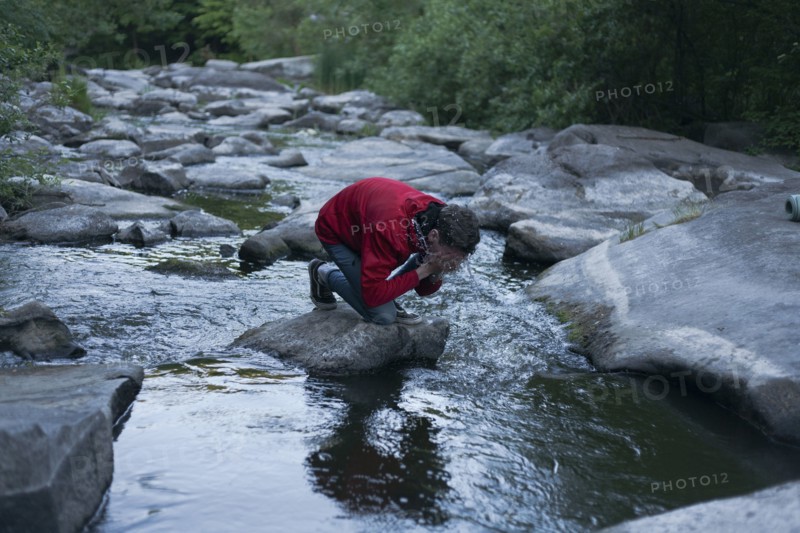 Caucasian man kneeling on rock in river splashing water on face