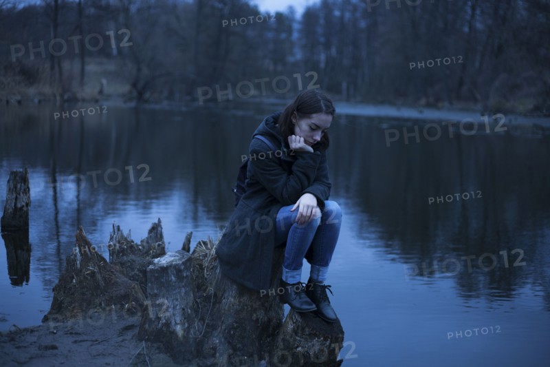 Caucasian woman sitting on tree stump near river thinking