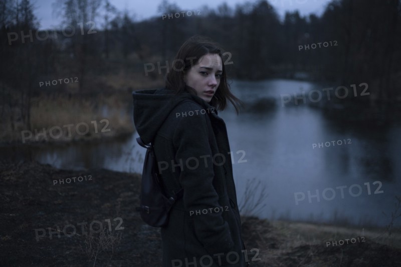 Portraits of serious Caucasian woman standing near river at night